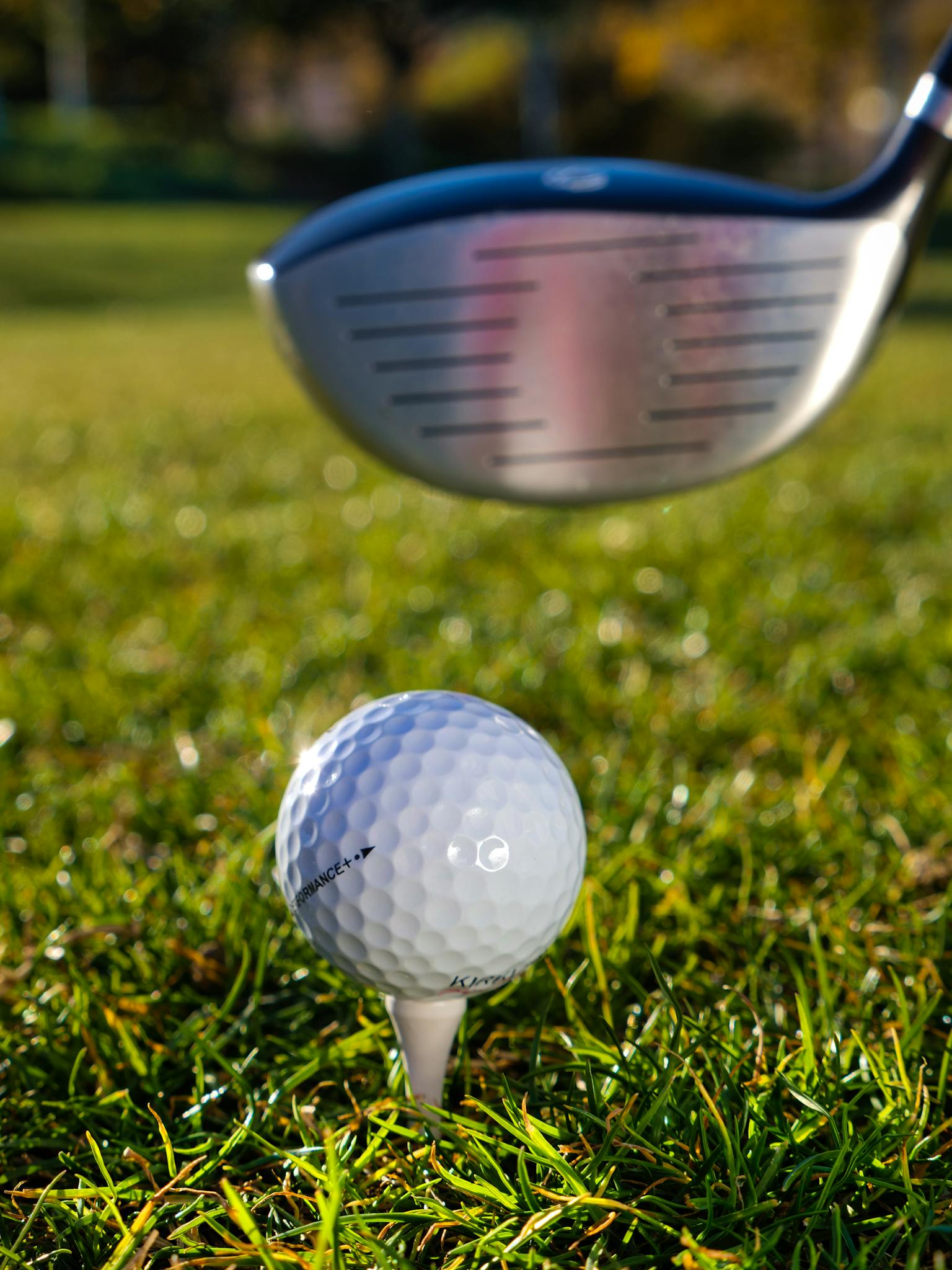 A close-up image showcasing a golf ball on a tee with a club on the grass, ready for a swing.