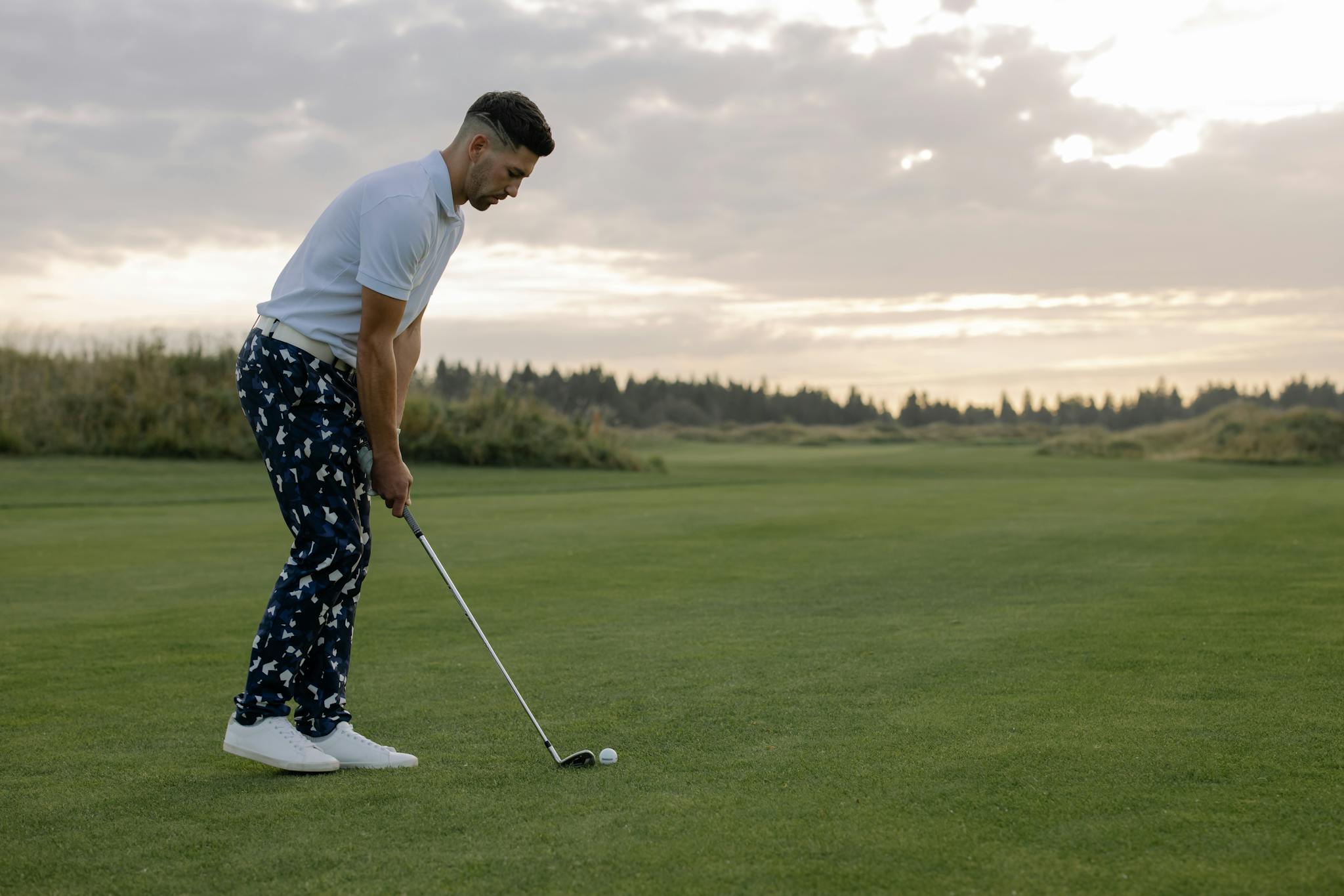 Professional golfer in action on a green field at sunset, showcasing focus and skill.